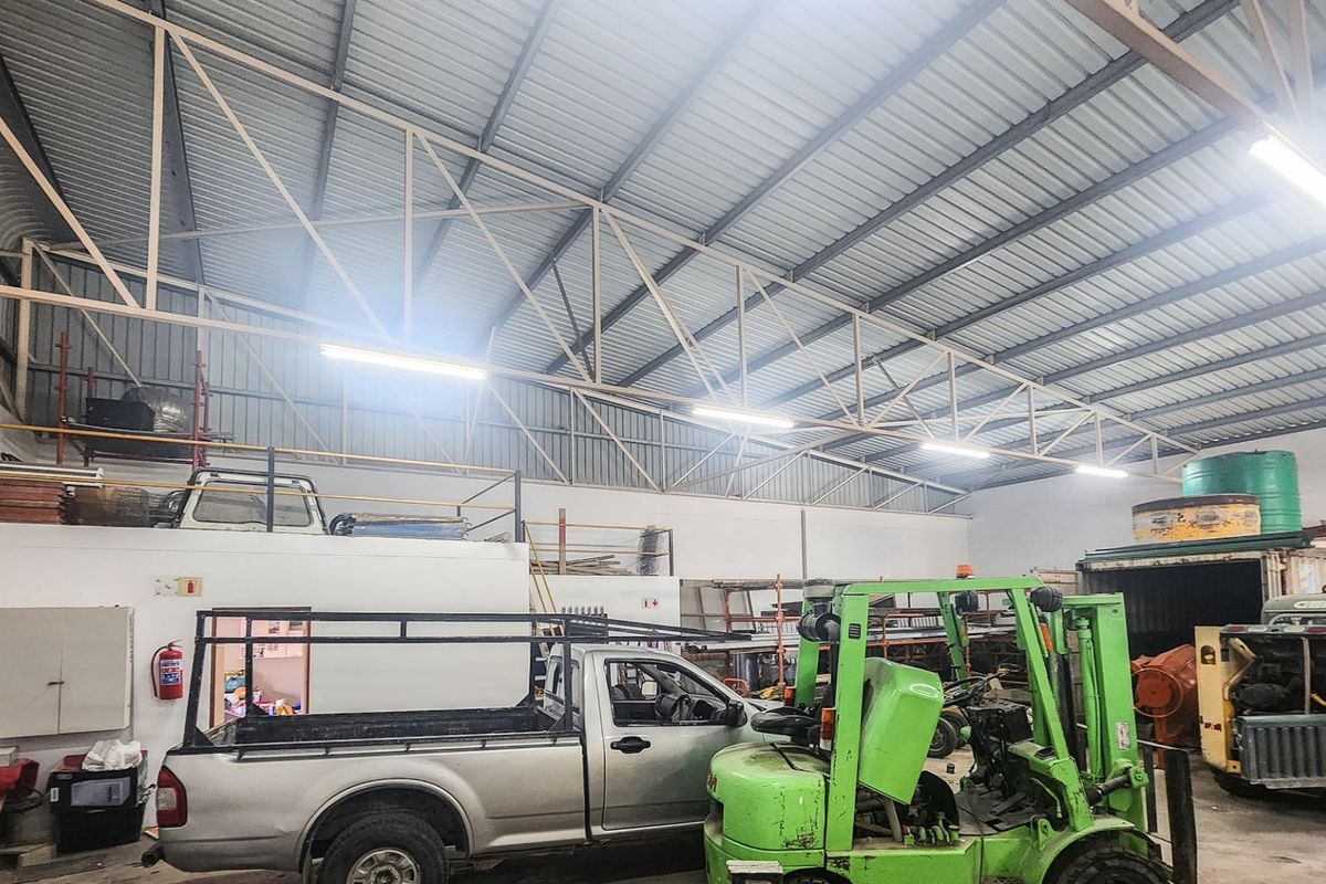 Spacious industrial warehouse featuring high ceilings with exposed steel trusses, corrugated metal roofing, and a functional mezzanine level for additional storage or workspace.