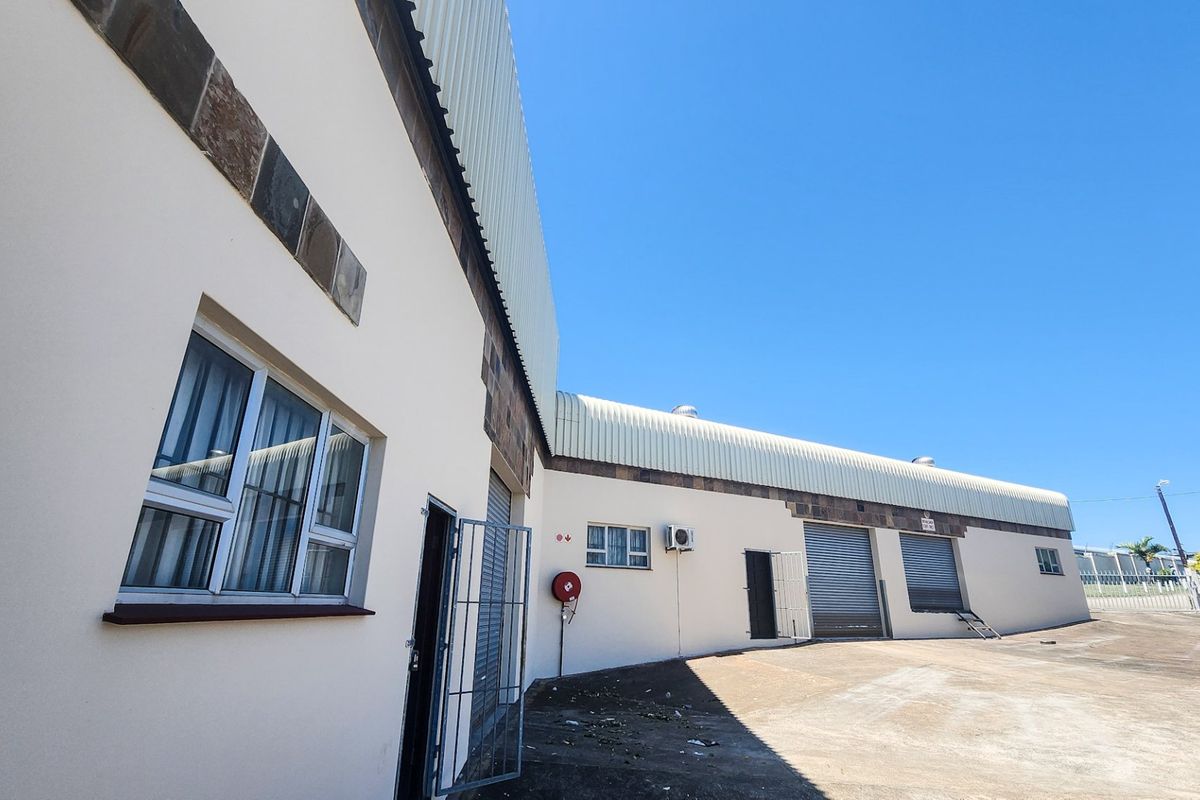 Rear view of an industrial property featuring a concrete yard, multiple roller shutter doors, security gates, and an external air conditioning unit.