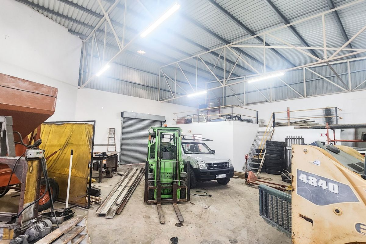Spacious industrial utility area featuring high ceilings with exposed steel trusses, a mezzanine level, concrete flooring, and a large roller shutter door.