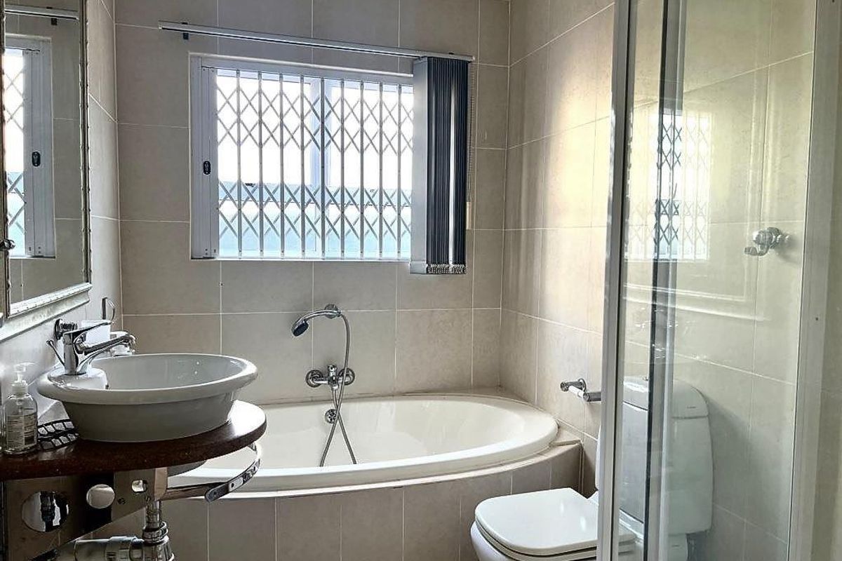 A well-maintained bathroom featuring a built-in bathtub, separate glass shower enclosure, vessel sink, and neutral ceramic wall tiling.