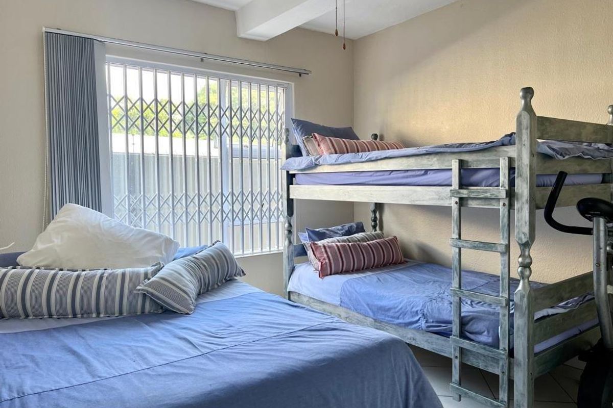 A bedroom featuring tiled flooring, a ceiling fan, and a window fitted with a security gate.