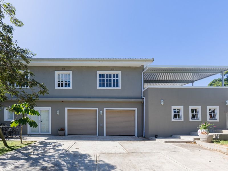 Front elevation of a two-story house featuring a double garage, concrete driveway, and a covered patio area with modern grey exterior finishes.