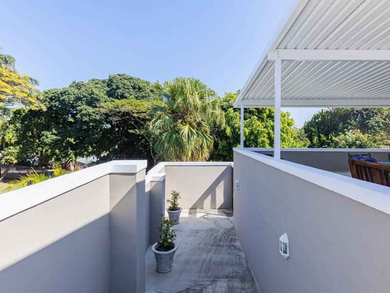 A well-maintained covered balcony featuring a clean parapet wall and outdoor lighting, offering an open-air space with views of the surrounding greenery.