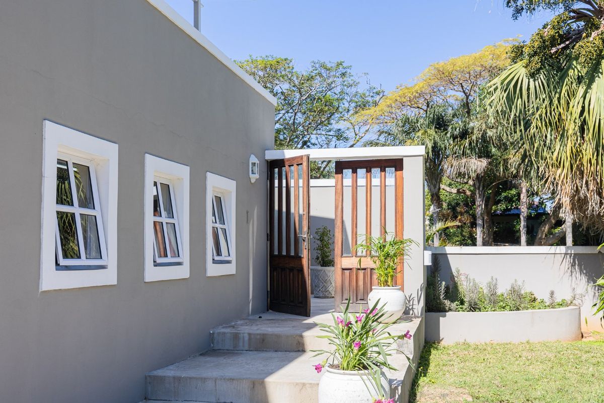 A well-maintained rear exterior view featuring concrete steps leading to timber-framed glass doors, set against a clean grey rendered wall and landscaped garden.