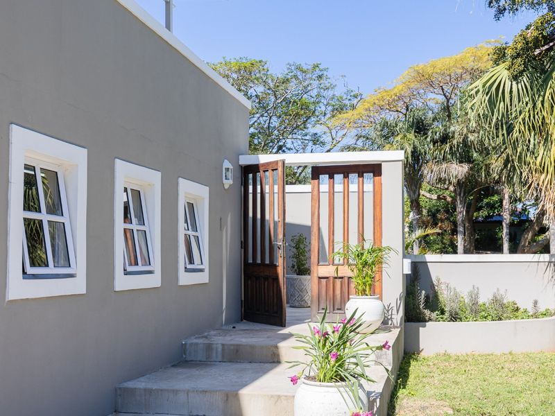 A well-maintained rear exterior view featuring concrete steps leading to timber-framed glass doors, set against a clean grey rendered wall and landscaped garden.