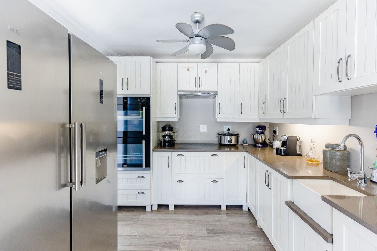 A well-appointed kitchen featuring white shaker-style cabinetry, stone countertops, a farmhouse sink, and integrated stainless steel appliances.