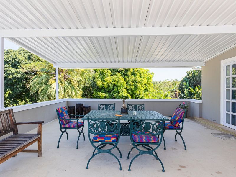 A spacious covered patio featuring a corrugated metal roof, concrete flooring, and direct access to the home through white-framed french doors.