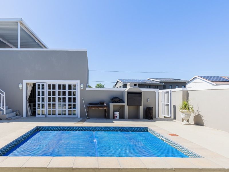 A well-maintained outdoor pool area featuring a paved deck, built-in braai, and direct access to the main dwelling via french doors.