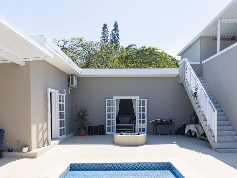 A spacious outdoor patio area featuring a swimming pool, central fire pit, and an external staircase leading to an upper level.