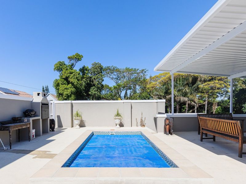 Outdoor pool area featuring a built-in braai, covered patio space, and a well-maintained swimming pool with a protective cover.