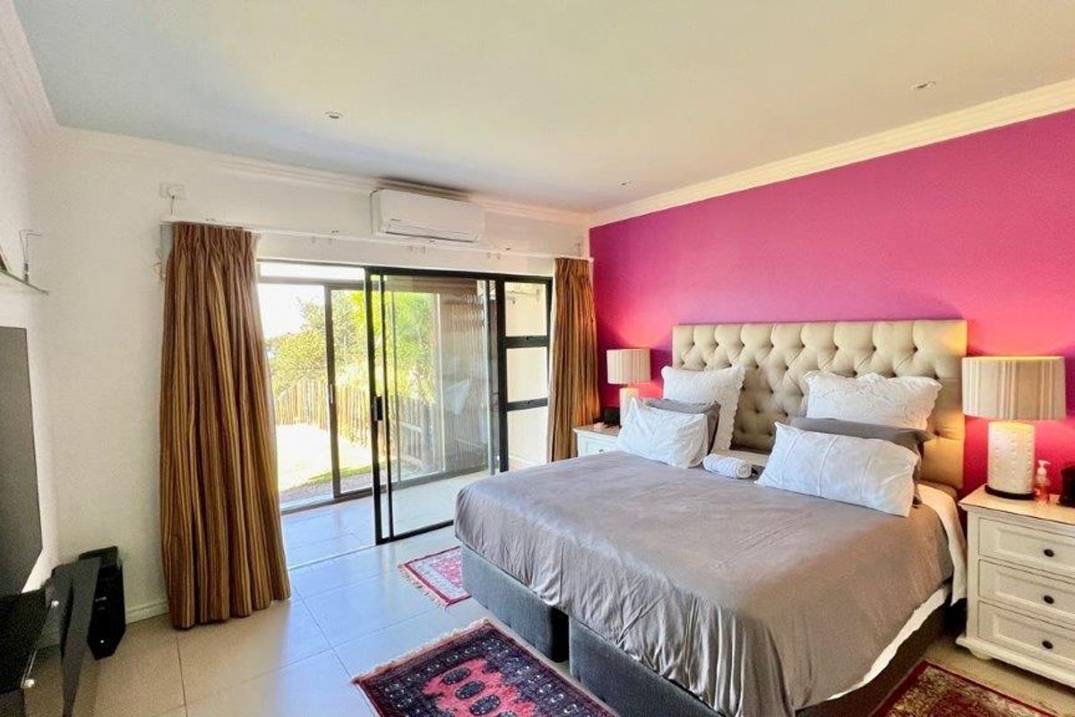 Spacious bedroom featuring tiled flooring, a wall-mounted air conditioning unit, and large sliding glass doors providing direct access to an outdoor patio area.