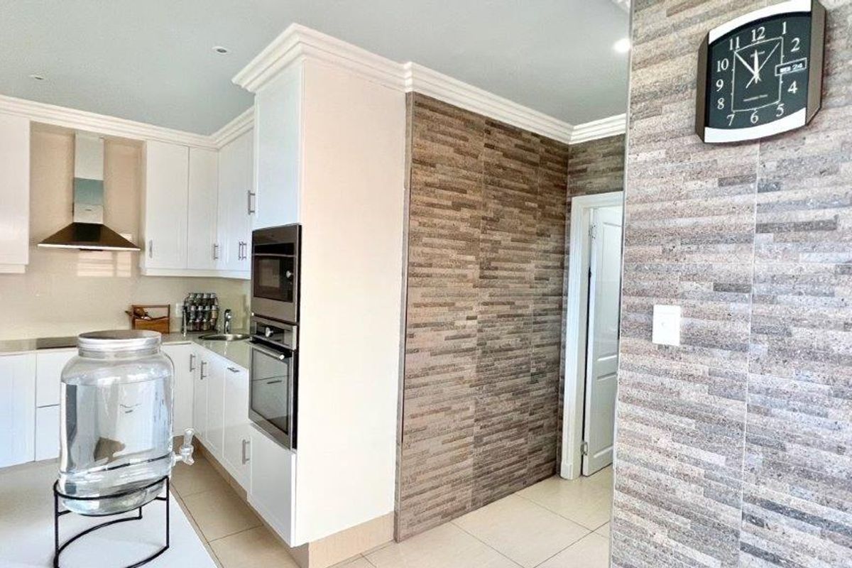 Modern kitchen featuring white cabinetry, built-in oven, extractor fan, and a decorative stone-cladding feature wall.