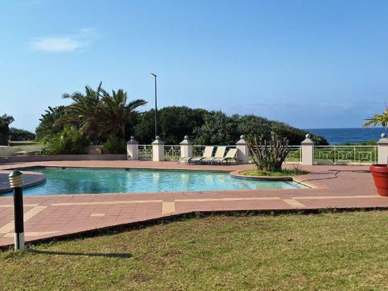 Communal swimming pool area featuring paved surround, built-in bar structure, and ocean views, set within a landscaped garden environment.