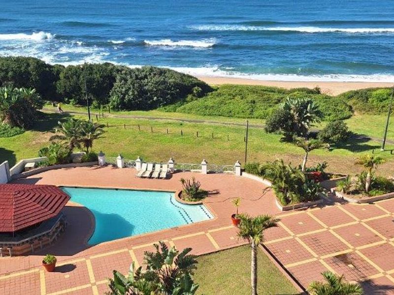Elevated view of the apartment complex pool area featuring a covered bar, paved terrace, and direct access to the coastal beachfront.