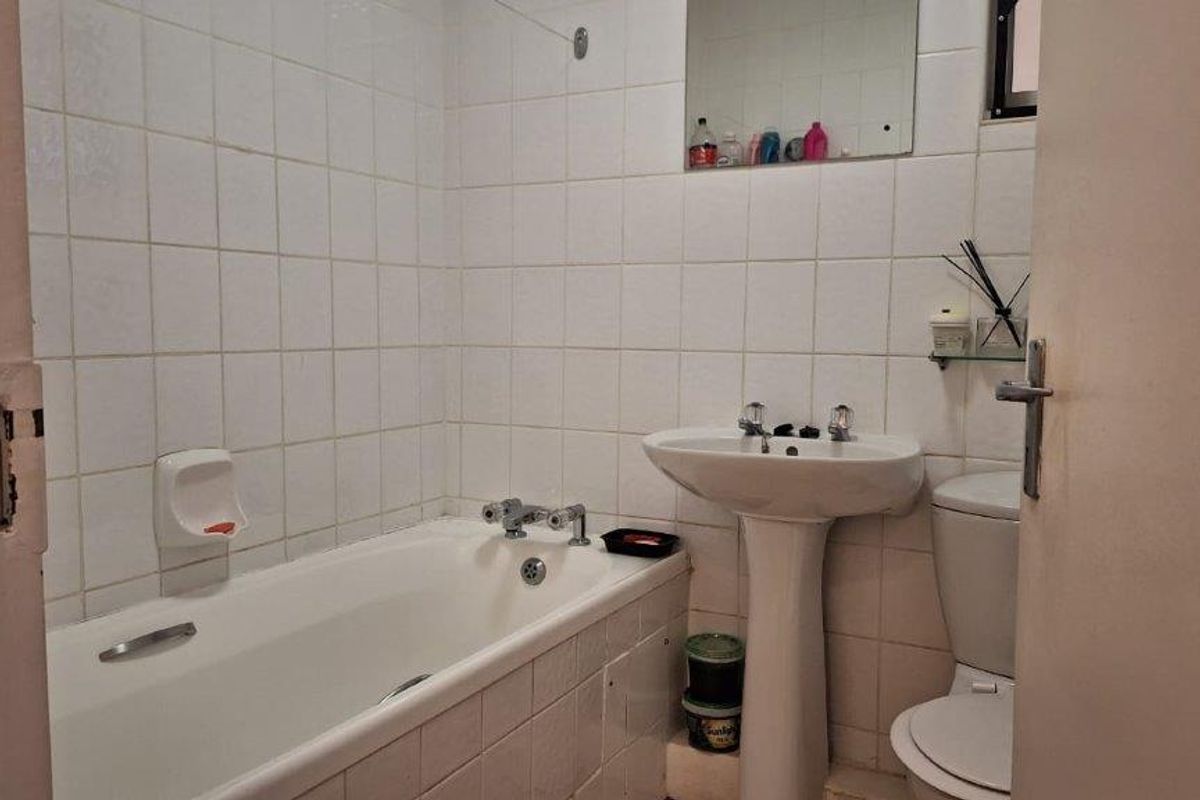 A dated bathroom featuring a standard bathtub, pedestal sink, and toilet with white wall tiling throughout.
