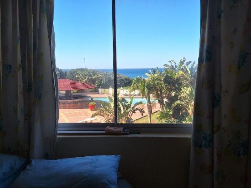 A view from a bedroom window overlooking a communal swimming pool area and the ocean beyond.