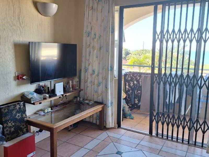 A living room featuring tiled flooring and a sliding door with security gate leading to a balcony with outdoor views.