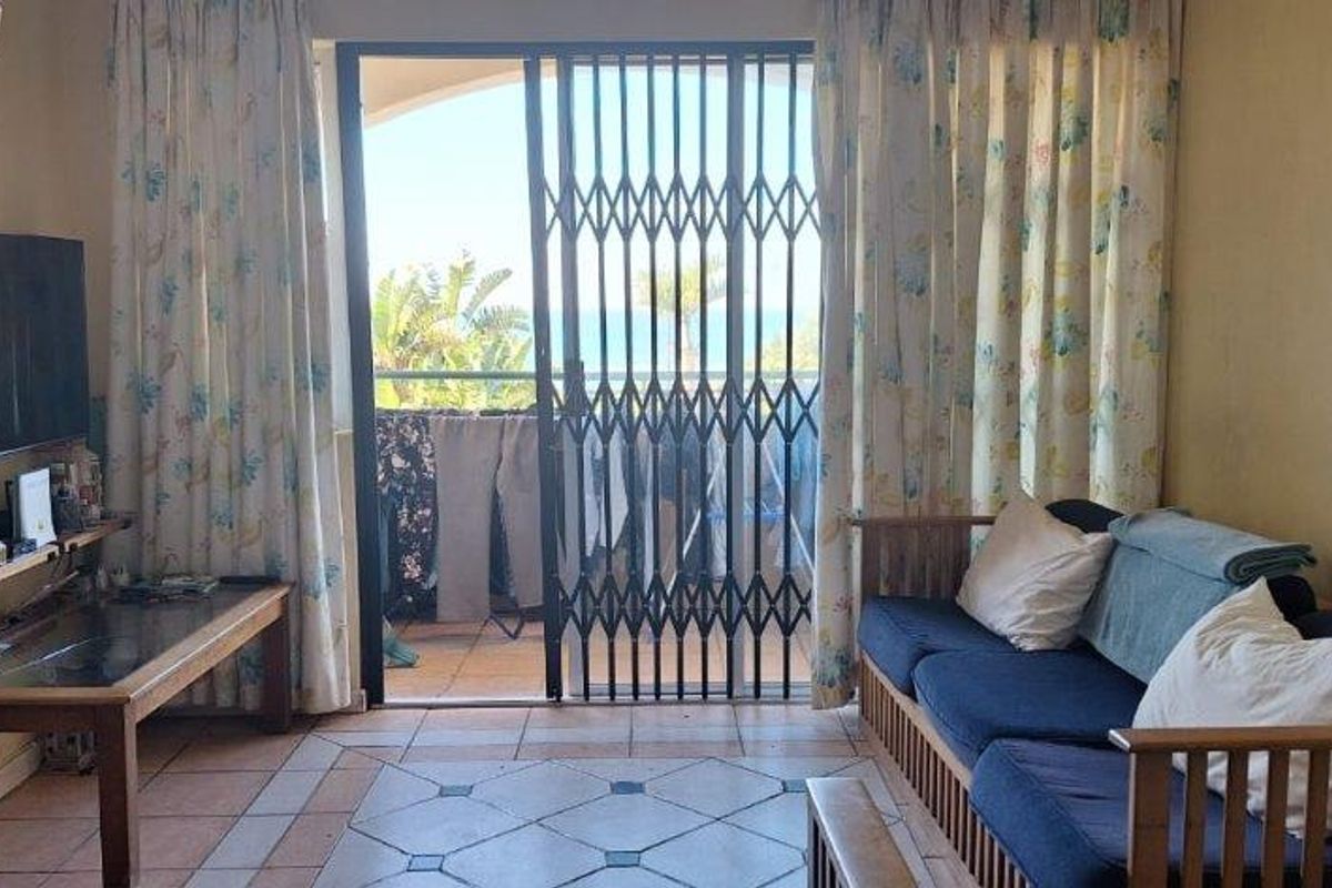A living room featuring tiled flooring and a sliding door leading to a balcony with security gate.