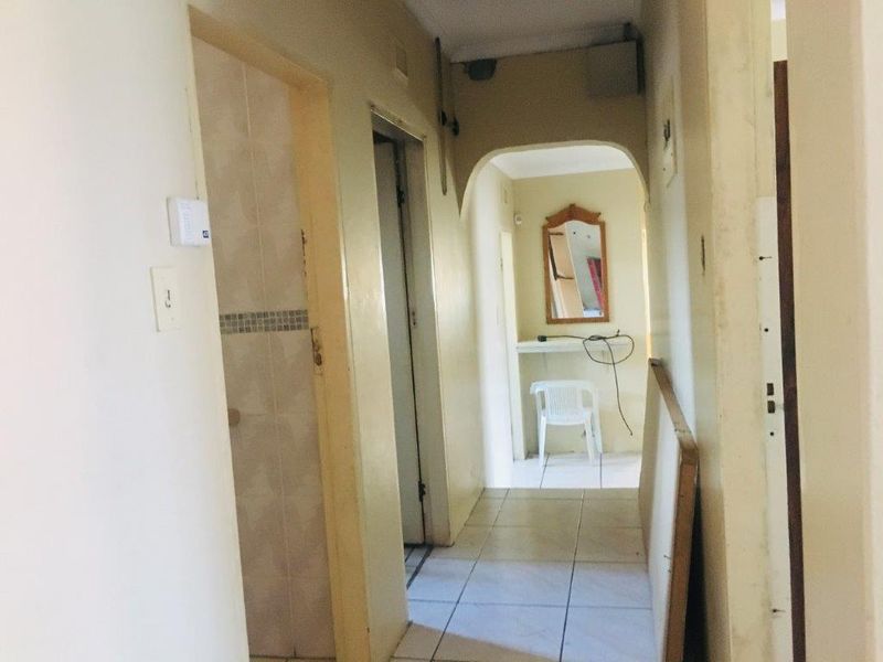 A functional hallway featuring tiled flooring and an arched transition leading to an additional space with built-in shelving.