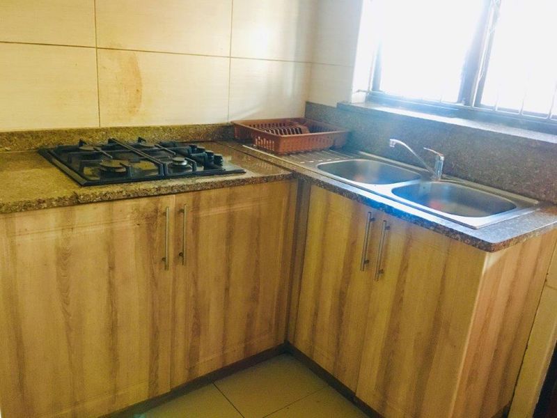 A functional kitchen area featuring wood-finish cabinetry, granite countertops, a built-in gas hob, and a double stainless steel sink.