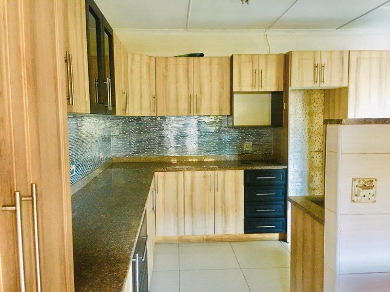A functional kitchen featuring laminate cabinetry, granite countertops, and a mosaic tile backsplash, with tiled flooring throughout.