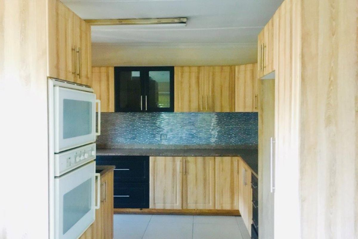 A functional kitchen featuring light wood-look cabinetry, dark accent cupboards, a tiled backsplash, and a built-in double oven.