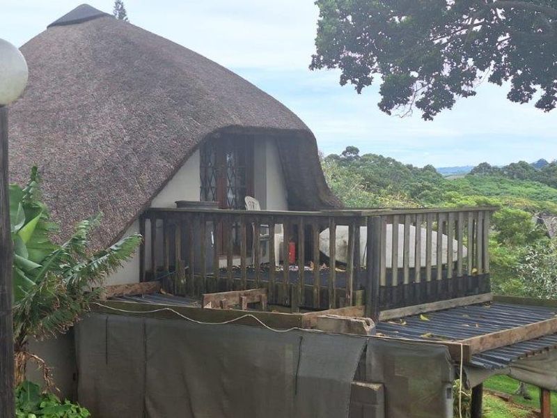 Exterior view of a townhouse featuring a traditional thatched roof and an elevated wooden balcony overlooking the surrounding landscape.
