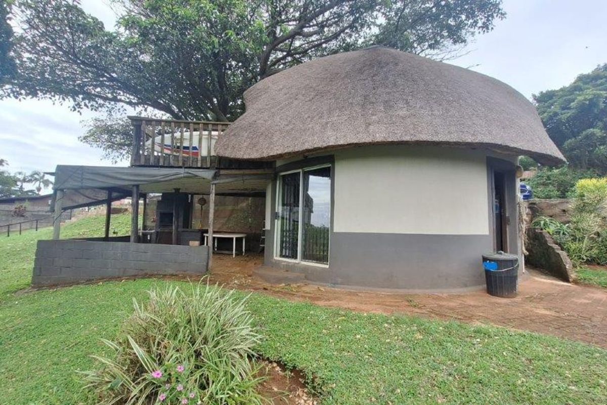 A unique circular townhouse unit featuring a traditional thatched roof, an attached covered patio area, and a raised wooden deck nestled under mature trees.