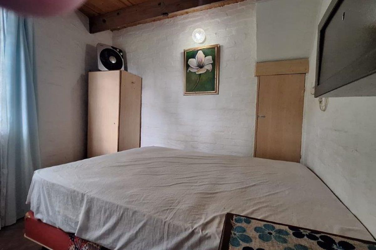 A compact bedroom featuring exposed timber ceiling beams, painted brick walls, and a built-in storage cupboard.