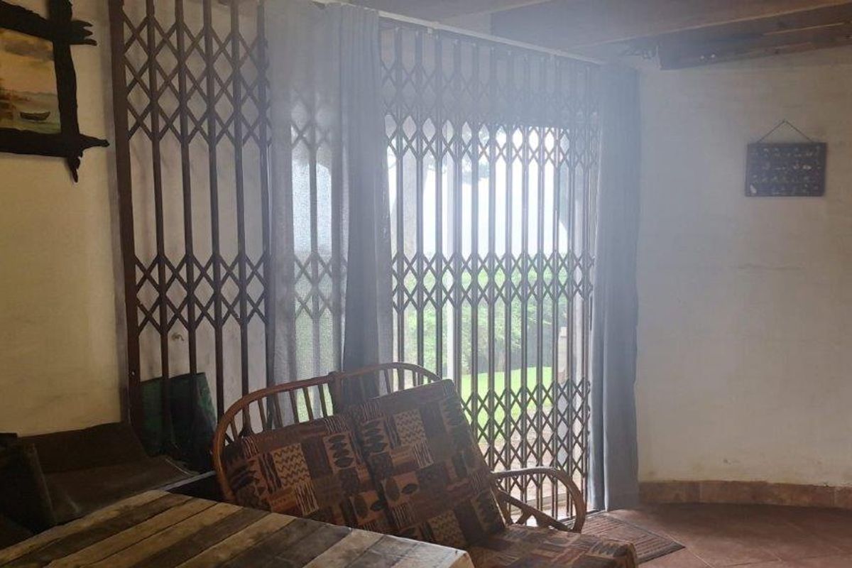 Living area featuring tiled flooring, exposed timber ceiling beams, and a security gate leading to the outdoor space.