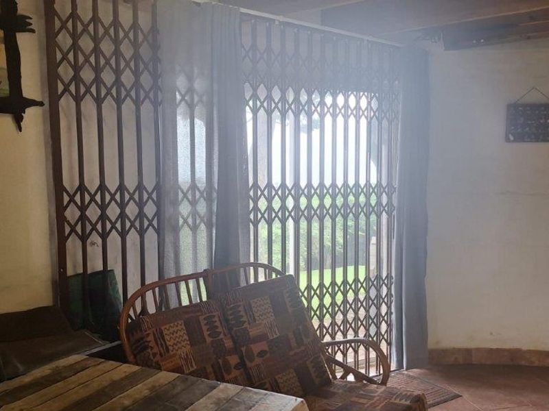 Living area featuring tiled flooring, exposed timber ceiling beams, and a security gate leading to the outdoor space.