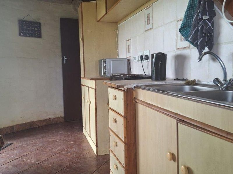 A dated kitchen area featuring original cabinetry, a double basin sink, and tiled splashbacks, offering potential for modernization and renovation.