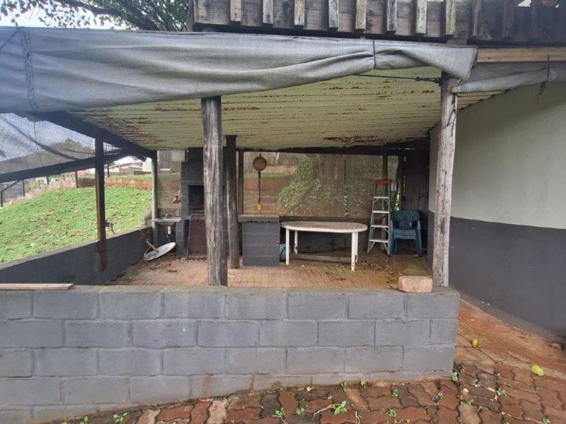 A covered outdoor patio area featuring a built-in brick braai, concrete block walling, and a corrugated metal roof structure in need of maintenance.