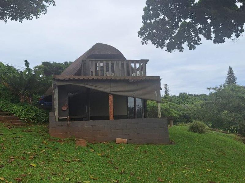 Rear view of a townhouse featuring a thatched roof, a wooden balcony, and a ground-level patio area set within a garden landscape.