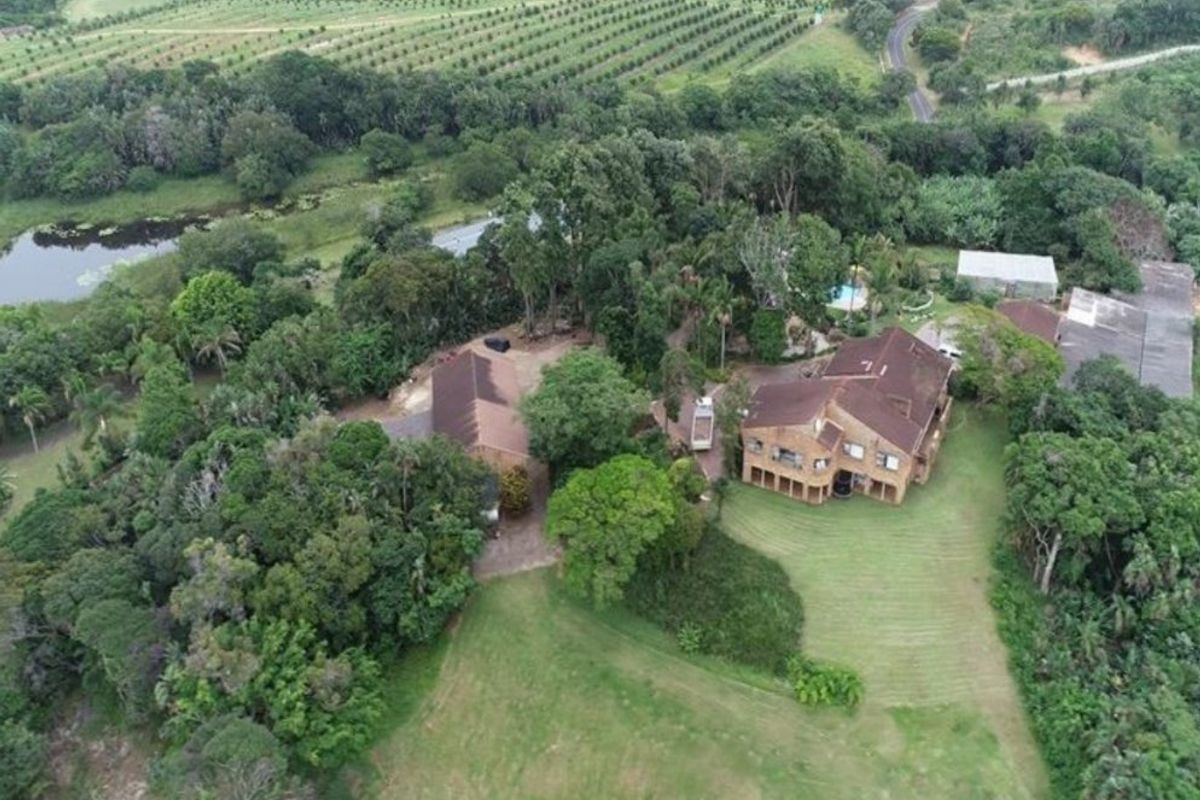 Aerial view of a large residential property featuring a multi-level house, outbuildings, swimming pool, and expansive surrounding gardens and natural landscape.
