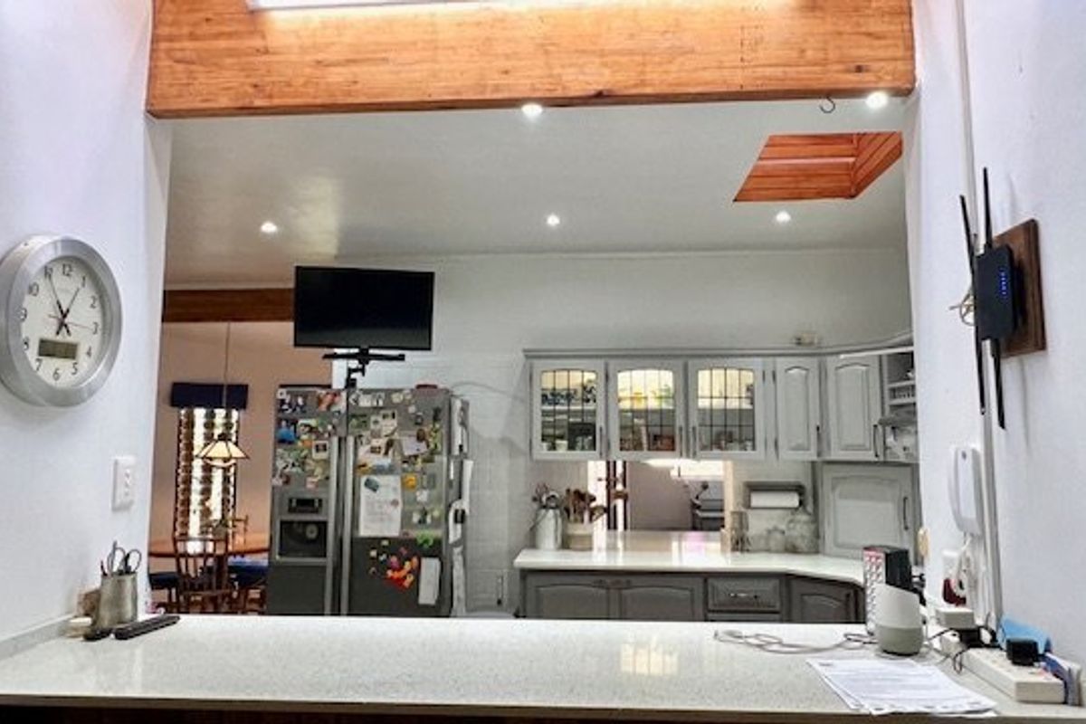 A functional kitchen featuring stone countertops, built-in cabinetry, and an exposed timber beam, with a view through to the adjacent dining area.
