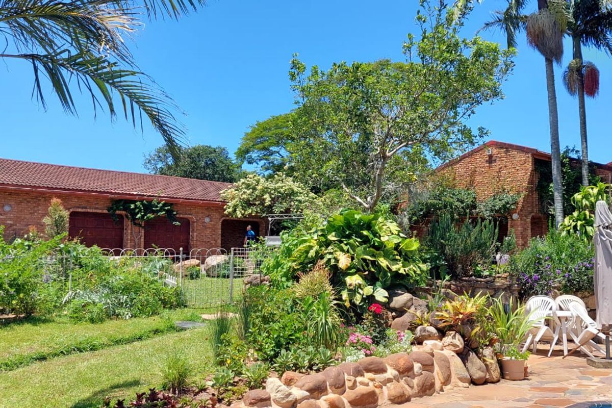 A view of the rear exterior featuring a brick house facade, stone retaining wall, paved patio area, and established garden landscaping.