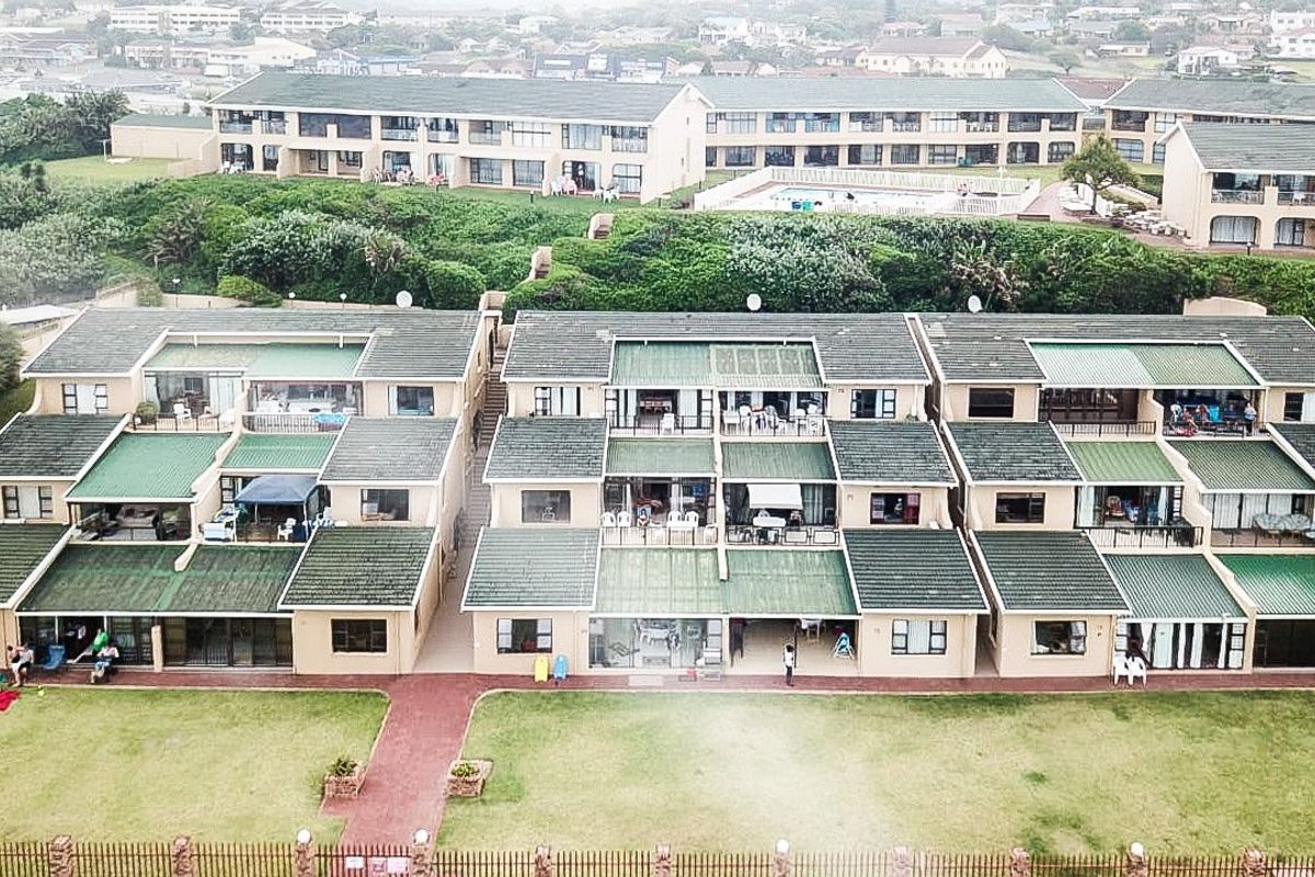 Aerial view of a multi-unit apartment complex featuring green tiled roofs, private balconies, and shared lawn areas within a coastal residential estate.