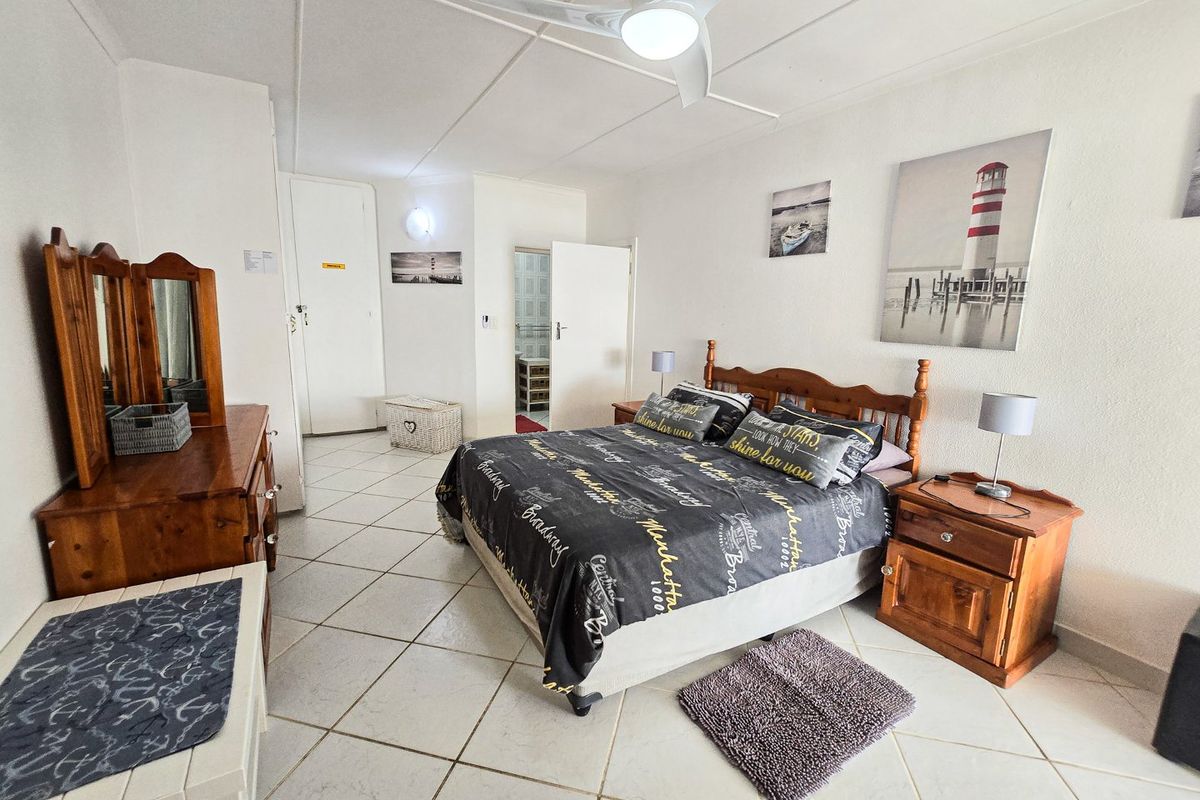 A spacious bedroom featuring tiled flooring, a ceiling fan, and direct access to an adjoining bathroom.