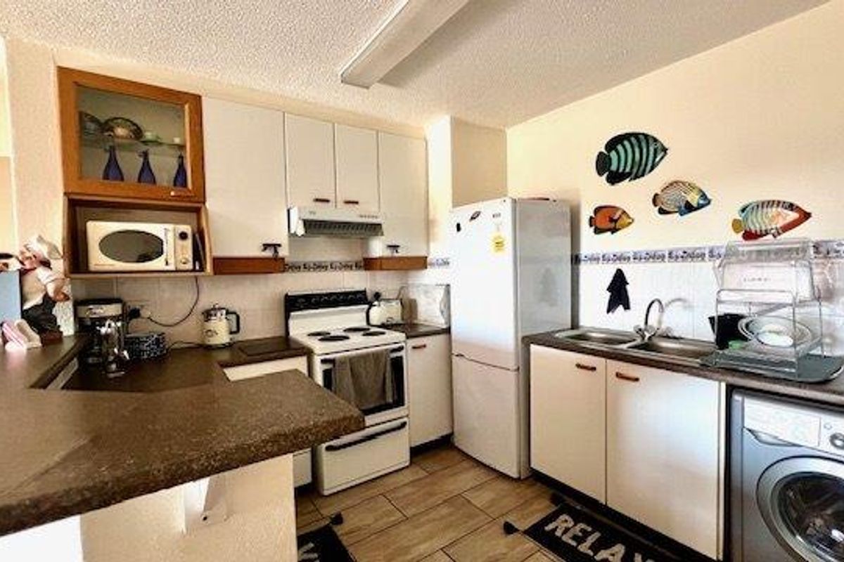 A functional kitchen featuring white cabinetry, laminate countertops, tiled backsplash, and integrated laundry plumbing, offering a practical layout for daily use.