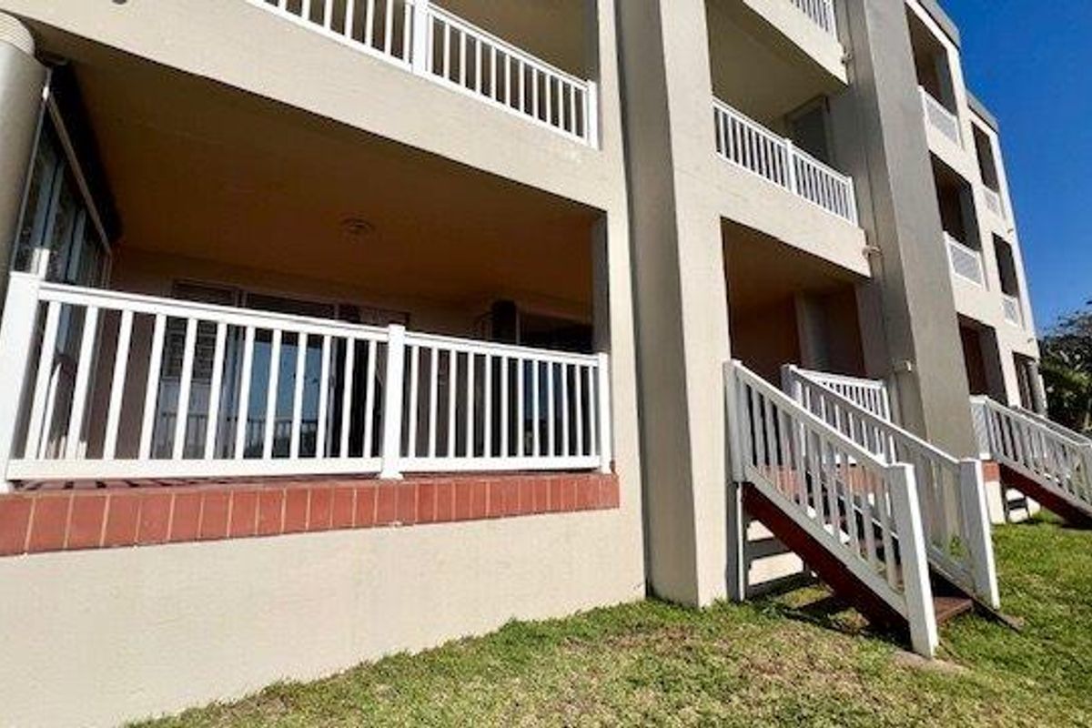 Rear view of the apartment building featuring ground floor balconies with white railings and external staircases leading to the lawn.