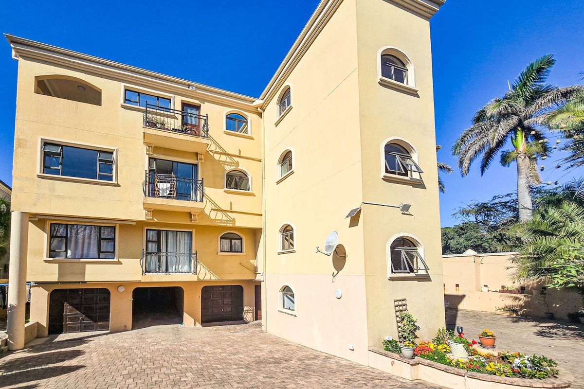 Rear view of a multi-story apartment building featuring paved driveway access, multiple balconies, arched windows, and integrated garage parking.