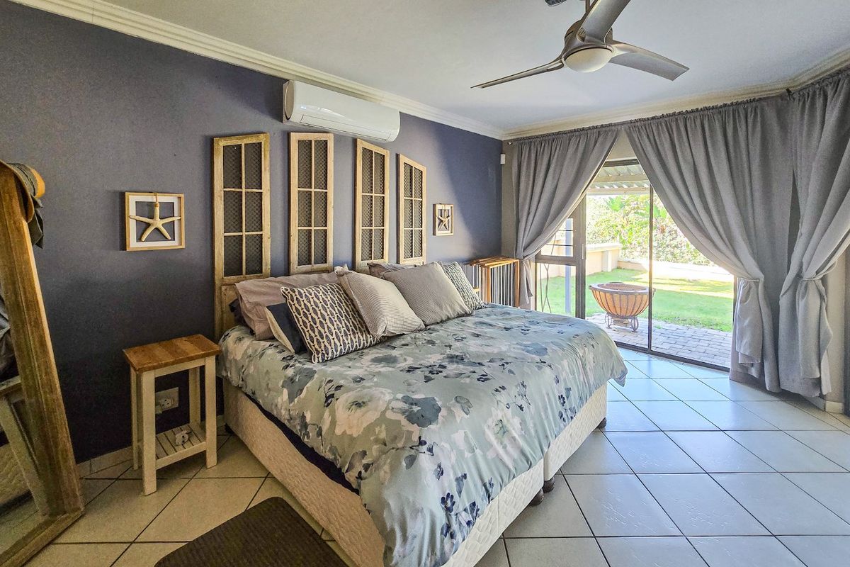 Spacious bedroom featuring tiled flooring, a ceiling fan, split-system air conditioning, and direct access to the outdoor patio through sliding glass doors.