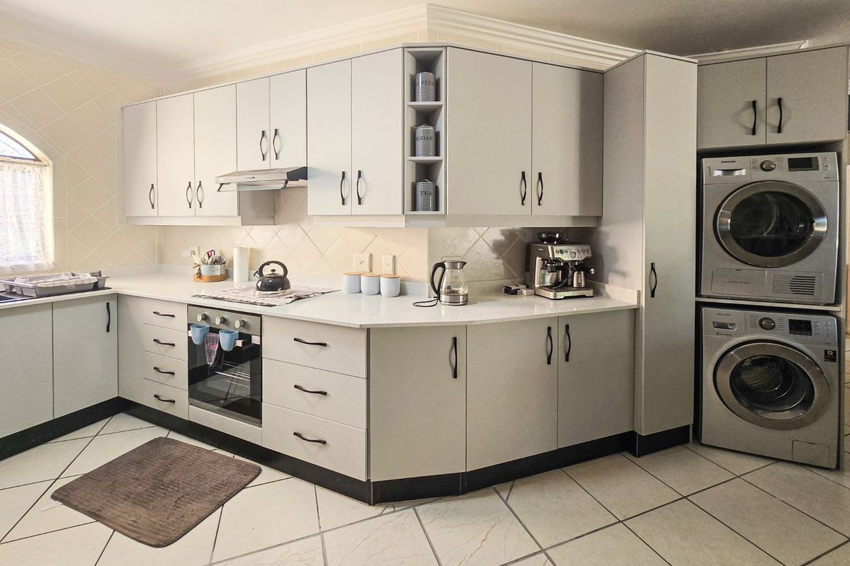 A well-maintained kitchen featuring light-toned cabinetry, stone countertops, built-in oven, extractor fan, and integrated laundry appliances with tiled flooring throughout.