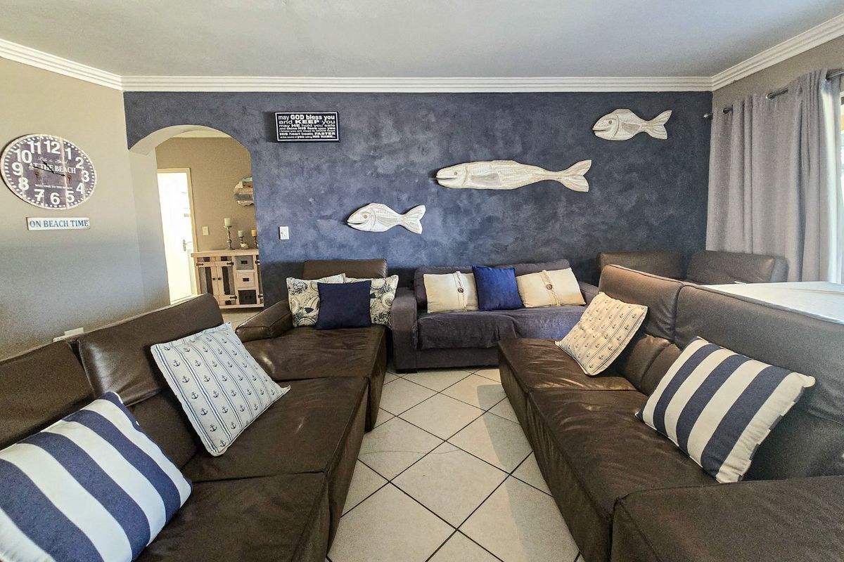 A living room featuring tiled flooring, decorative cove cornicing, and a feature wall with an arched entryway leading to an adjacent space.