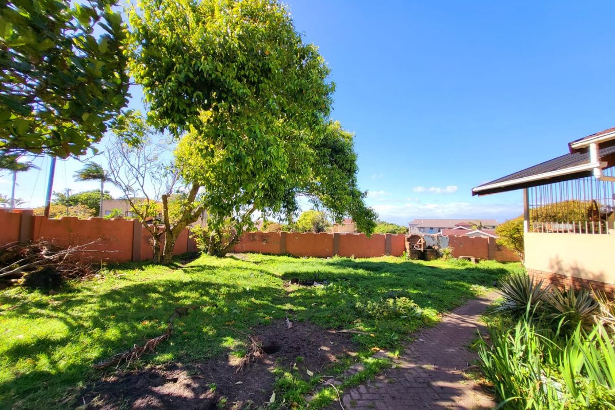 A spacious rear garden area featuring a paved walkway, mature trees, and a perimeter boundary wall, offering potential for landscaping and outdoor improvement.
