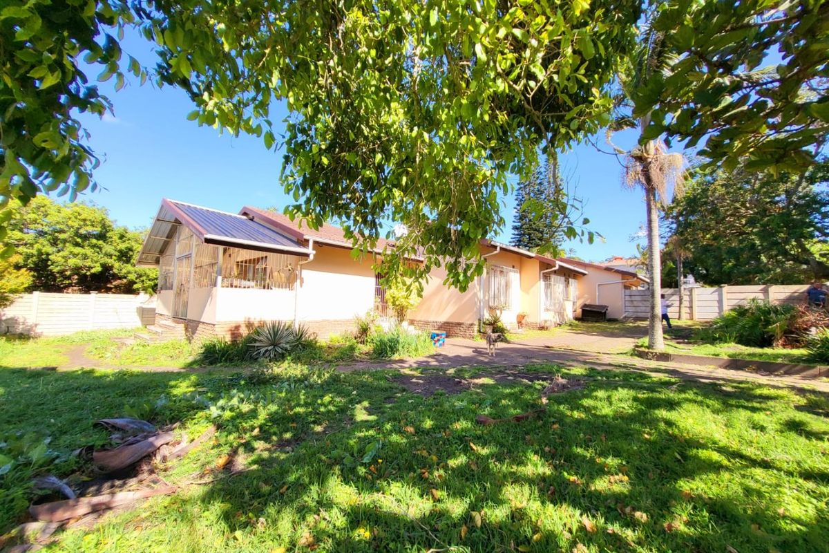 A view of the rear exterior of the house, featuring a paved patio area, established garden, and perimeter boundary walling.