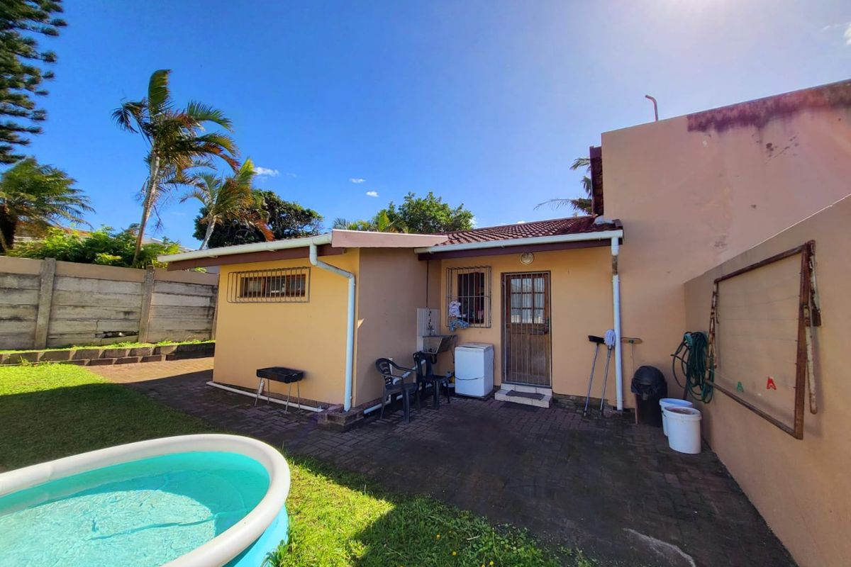 Rear exterior view of the property featuring a paved patio area, security-gated entrance, and access to the garden and pool area.