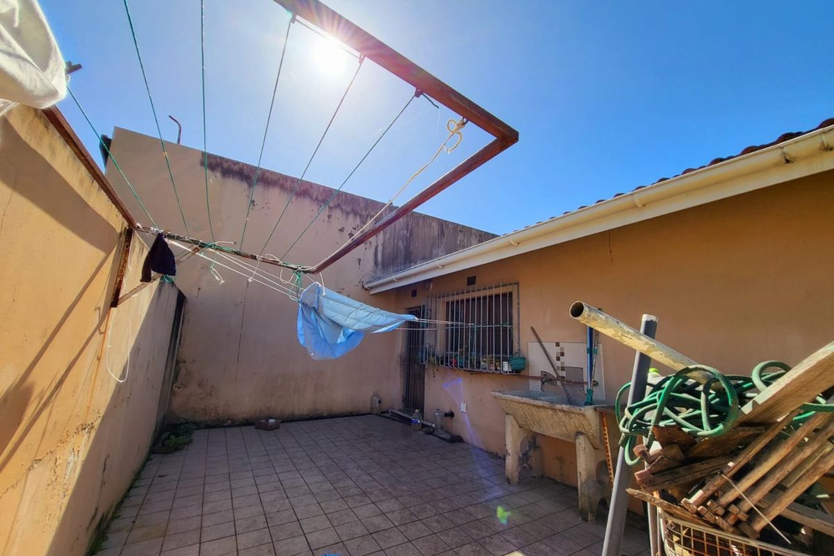 A functional rear courtyard area featuring a concrete utility sink, tiled flooring, and a wall-mounted clothes drying rack.