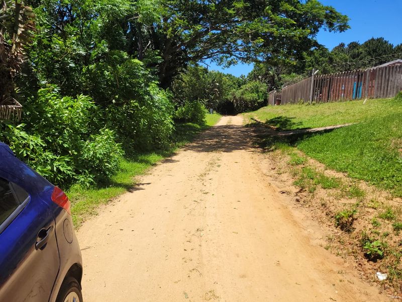 A view of an unpaved dirt access road bordered by mature trees and perimeter fencing on a residential property.